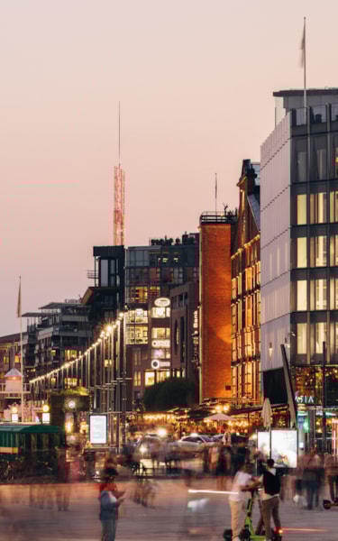 Kveld ved Aker Brygge med moderne bygninger, travelt byliv og en båt til kai ved vannkanten.