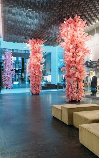 Close-up of a stylish indoor shopping area with pink artificial trees, modern ceiling, and store displays.